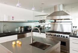 English feared the mirrored wall would collect water splashes if continued behind the sink. So he sandblasted it and tucked it under a long stainless steel shelf. It reflects light back onto the black granite and contributes a feeling of greater depth to