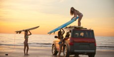 girls at beach putting surfboards on car top