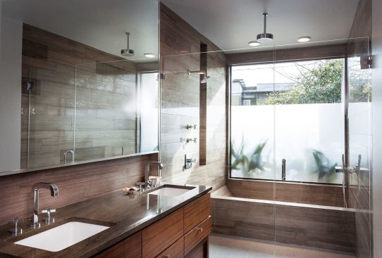 Here, the bath tub is contained within the glass-walled shower. A ceiling height picture window that's frosted lets the outdoors in while ensuring privacy.