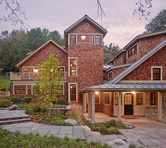 Inspired by its natural surroundings, this family escape in the woods of Massachusetts is sided with local stone and cedar shingles interspersed with plenty of oversized windows that allow for a New England farm house feel while maintaining plenty of natural light. Window treatments sport black clad exteriors to complement the natural materials and standing seam metal roof. Inside, window casements are done in Douglas fir to match exposed beams and millwork. Project: Family Retreat, Tyringham, Mass.; Architect: Solomon+Bauer+Giambastiani Architects, Watertown, Mass.