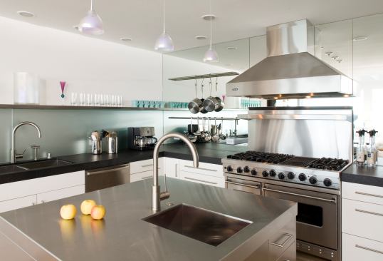 This sleek residential kitchen offers the sturdy utility of a commercial one thanks to a stainless steel island, an oversized range and hood, and exaggerated gooseneck faucets. Overhead lighting fixtures made to look like sodium lamps complete the industrial aesthetic. Project: Sausalito Residence, Sausalito, Calif.; Builder: Landmark Builders, Novato, Calif.; Architect: Mark English Architects, San Francisco