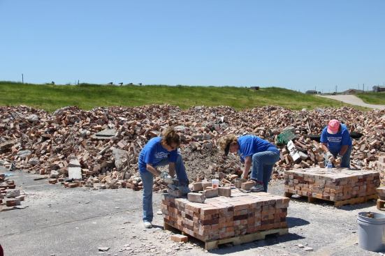 Volunteers with Presbyterian Disaster Assistance, visiting from Kansas, chip the mortar from hundreds of bricks at the site of the destroyed Joplin High School. Bricks will be printed with an image of the planned new school and sold for donations to help with the rebuilding.