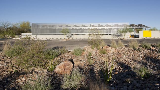 AFTER: The west fa&ccedil;ade, which includes the entry, after the renovation. This area was of prime concern because western exposure in Arizona means intense solar heat gain and glare. The painted steel fa&ccedil;ade provides shade, supports new solar panels, screens rainwater collection cisterns, and makes a bold and modern statement. PRODUCTS: Galvalume siding.