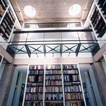 Four existing circular skylights flood the library with natural daylight while industrial task lights illuminate the stacks at night.