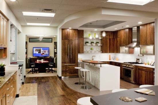 The main kitchen at Melton Construction’s Design Studio features the popular look of dark woods against white surfaces. Flat panel walnut cabinets and gray-toned wood floor play against a white waterfall countertop and metal cabinets. Builder: Melton Construction, Denver; Design Studio: Success Strategies; Merchandiser: In-house