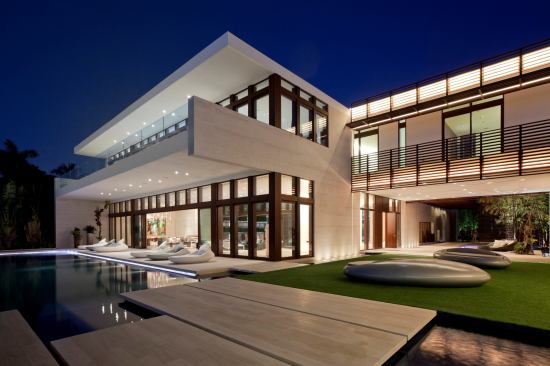 Seen from the rear, the home features laminated mahogany&nbsp;windows and door frames, water elements, and a glass-fronted second level. The&nbsp;metal brise-soleil, canopies, and louvered walls&nbsp;feature a&nbsp;powder-coated paint in a woodgrain texture.&nbsp;
