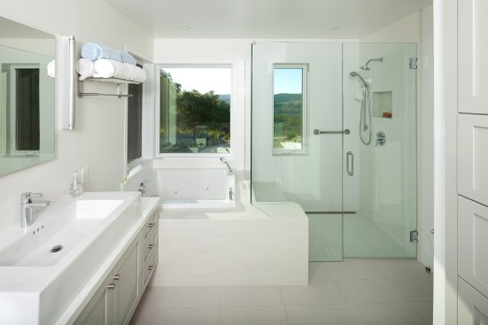 The all-white finishes, glass shower panels, and square fixtures create a modern feel in this bath.&nbsp;Project: Arroyo Grande Modern Farmhouse by Gast Architects