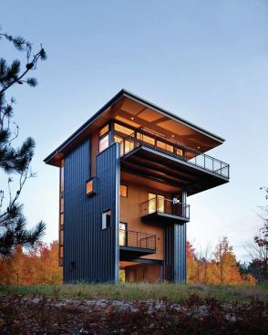 The vertically organized building reads as a plywood volume suspended between two metal-clad walls.