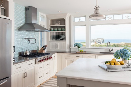 White cabinets make this kitchen feel modern, but the blue-tiled backsplash adds vibrancy to the space. Large windows flood this beach-side kitchen with natural light.&nbsp;Project: Cape Cod Beach House by REEF&nbsp;