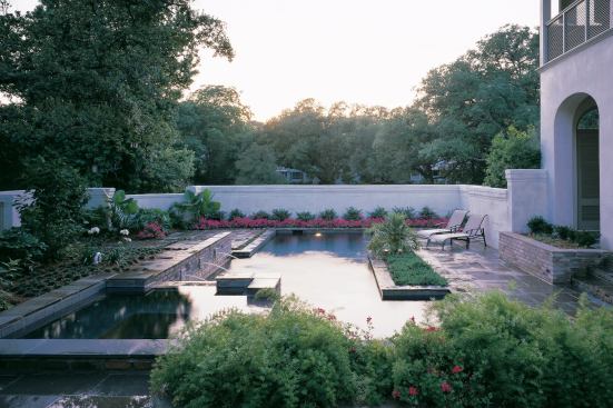 Nestled into the crook of an L-shaped home, this small urban courtyard offers the owners privacy from the world outside its concrete block walls and the easy-care advantage of hardscaped surfaces. The bluestone paving and used brick planters are softened by low-maintenance plantings and the splash of water spilling from the spa into the pool below it.