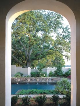 From its elevated position, the veranda encompasses much more than the courtyard. Its arches frame a layered scene of plantings, pool, fountain, and beyond the fence to ancient live oaks and the lake.