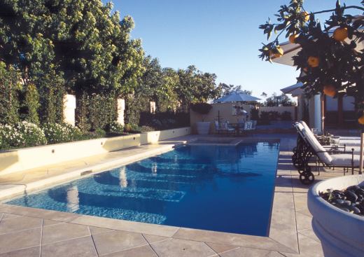 Most of this suburban backyard has been designed to provide functional outdoor rooms that flow easily from indoor counterparts. Here, the home’s family room leads to a covered porch, the outdoor kitchen and dining area, and the pool and spa.