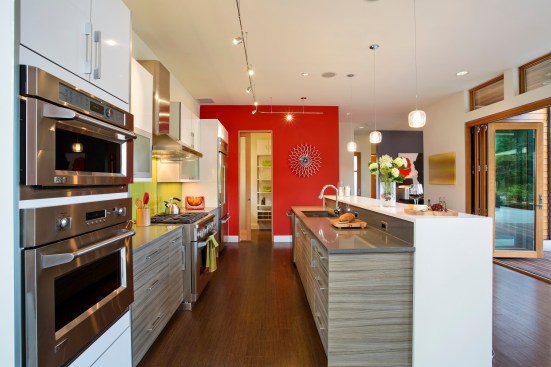 Both the red wall and lime-green backsplash in this kitchen provide colorful focal points in a small space.&nbsp;Project: EVOKE-LUXE by Quadrant Homes&nbsp;