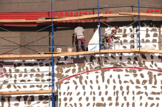 Workers stucco a new office building near the Huddlestons’ house.