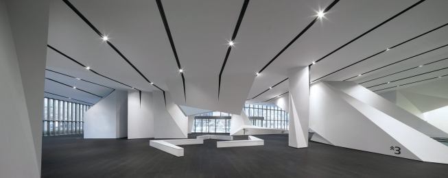 The ground floor of the Model Home Gallery showcases the ceiling detail designed by NADAAA. Black-painted channels inscribed in the ceiling plane (which consists of white Venetian plaster on gypsum board) house systems, including lighting, sprinklers, 

and HVAC. 