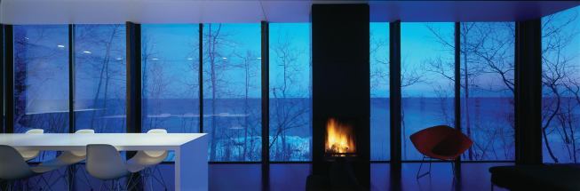 A white dining table runs through the main house, parallel to Lake Superior. The home’s quiet design directs attention to the lake year-round, at all times of day.